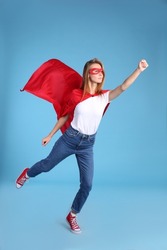 Confident woman wearing superhero cape and mask on light blue background