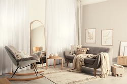 Stylish living room interior with large mirror, comfortable sofa and rocking chair