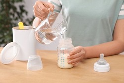 Woman preparing infant formula at table indoors, closeup. Baby milk
