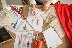Fashion designer creating new clothes in sketchbook at wooden table, top view