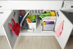 Different cleaning tools and supplies in open cabinet under sink