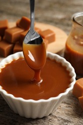 Taking tasty salted caramel with spoon from bowl at wooden table, closeup