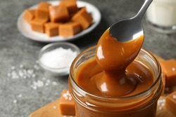Taking yummy salted caramel with spoon from glass jar at table, closeup. Space for text