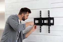 Man with screwdriver installing TV bracket on wall indoors