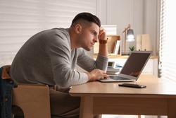 Man with poor posture using laptop at table indoors
