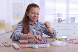 Cute girl making beaded jewelry at table indoors