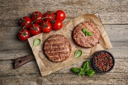 Tasty grilled hamburger patties with cherry tomatoes and seasonings on wooden table, flat lay