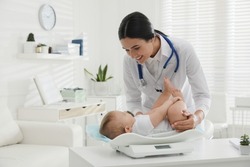 Young pediatrician weighting cute little baby in clinic