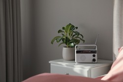 Stylish radio receiver and plant on nightstand in bedroom