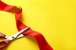 Red ribbon and scissors on yellow background, top view. Space for text