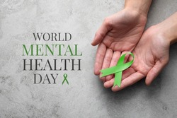 World Mental Health Day. Woman holding green ribbon at grey table, top view