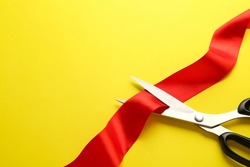 Red ribbon and scissors on yellow background, top view. Space for text