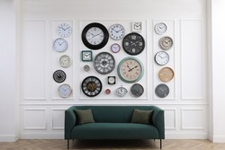 Collection of different clocks and comfortable sofa in stylish room. Interior design