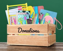 Donation box with different school stationery on wooden table near chalkboard