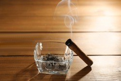 Smoldering cigar near glass ashtray on wooden table
