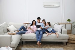 Happy family resting under air conditioner on white wall at home