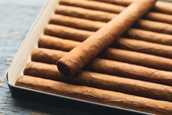 Many cigars in box on grey wooden table, closeup