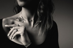 Young woman with tattoo on dark background, closeup. Black and white photography