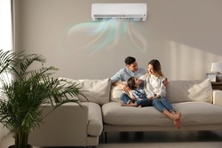 Happy family resting under air conditioner on beige wall at home