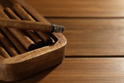 Many cigars in box on wooden table, closeup. Space for text