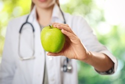 Nutritionist with fresh apple on blurred green background, closeup