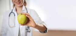 Nutritionist with fresh apple in her office, closeup view with space for text. Banner design
