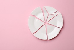 Pieces of broken ceramic plate on pink background, flat lay. Space for text