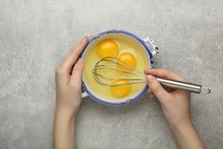 Woman whisking eggs at grey table, top view