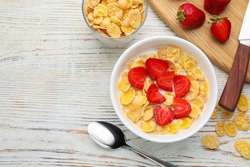 Bowl of tasty crispy corn flakes with milk and strawberries on white wooden table, flat lay. Space for text