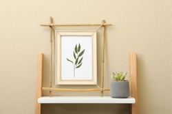 Bamboo frame and green plant on shelving unit near beige wall