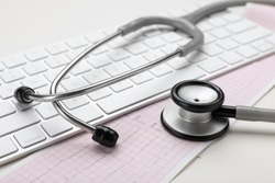 Keyboard, cardiogram paper and stethoscope on beige background, closeup