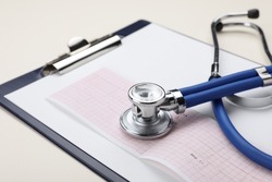 Stethoscope, clipboard and cardiogram paper on beige background, closeup