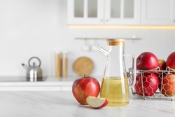 Natural apple vinegar and fresh fruits on white marble table in kitchen. Space for text