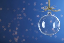 Transparent glass Christmas ball with golden ribbon and bow against blue background. Space for text