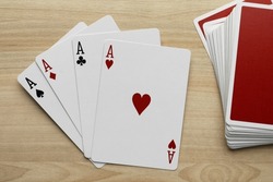 Four aces and deck of playing cards on wooden table, flat lay