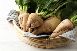 Basket with fresh sugar beets on white wooden table, closeup