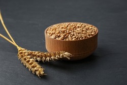 Dried ears of wheat and grains in wooden bowl on black table
