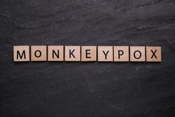 Word Monkeypox made of wooden squares on black background, top view