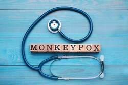 Word Monkeypox made of cubes and stethoscope on light blue wooden table, flat lay