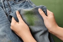 Woman holding jeans with stain on green background, closeup