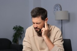 Man suffering from ear pain on in room