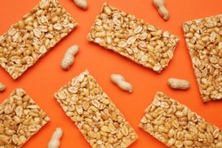 Tasty kozinaki bars and peanuts on orange background, flat lay