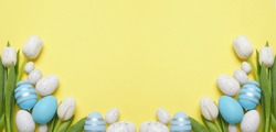 Flat lay composition with decorated Easter eggs and flowers on pale yellow background, space for text. Banner design