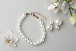 Elegant pearl earrings, bracelet and orchid flowers on white background, flat lay