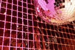 Shiny disco ball against foil party curtain under pink light, space for text