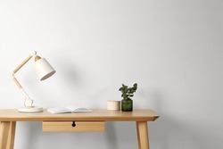 Stylish modern desk lamp, open book and plant on wooden table near white wall, space for text