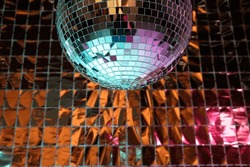 Shiny disco ball against foil party curtain under turquoise and orange light. Space for text