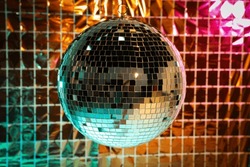 Shiny disco ball against foil party curtain under turquoise and orange light
