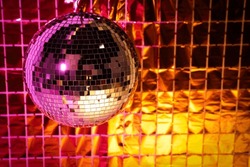 Shiny disco ball against foil party curtain under pink and orange light. Space for text