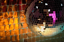 Shiny disco ball against foil party curtain under orange light. Space for text